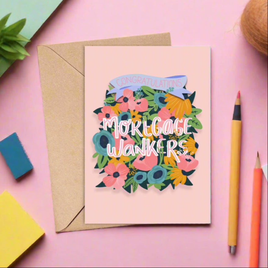 Card with floral design and text on a pink background with stationery items.